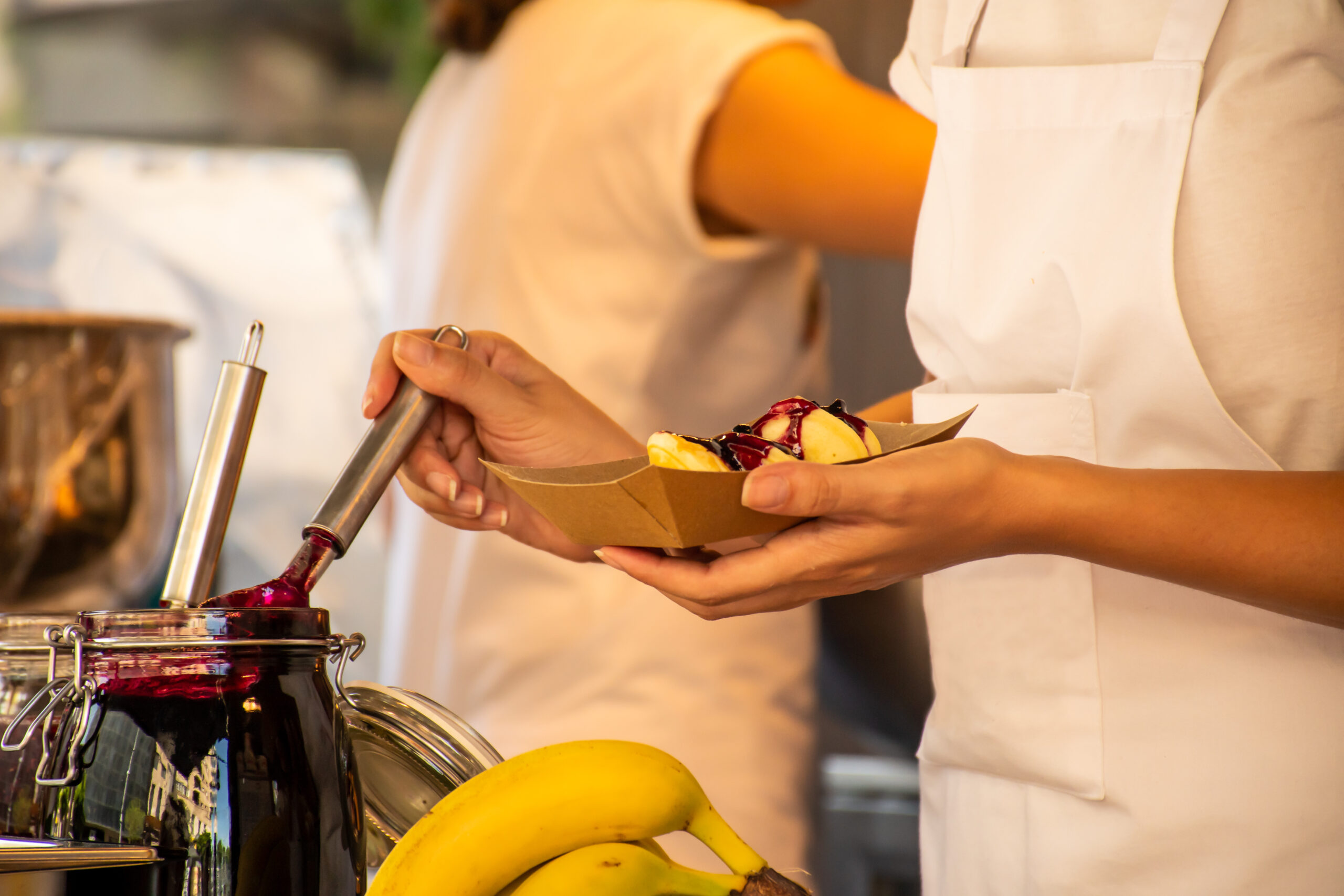 donut food truck employee pouring sweet fruit jam on top of the donuts