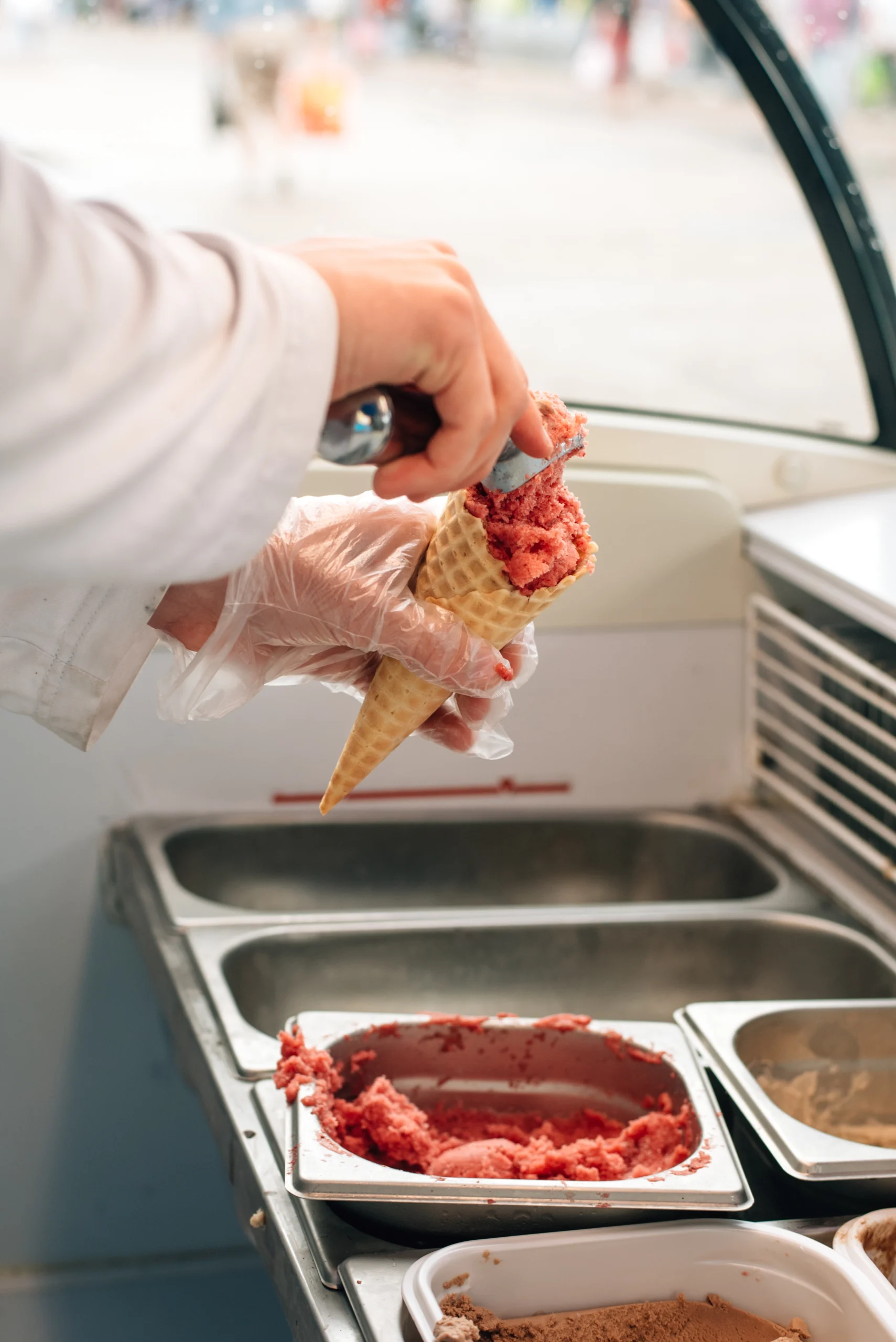 A close-up of a vendor scooping fresh strawberry ice cream into a waffle cone inside a well-equipped ice cream truck