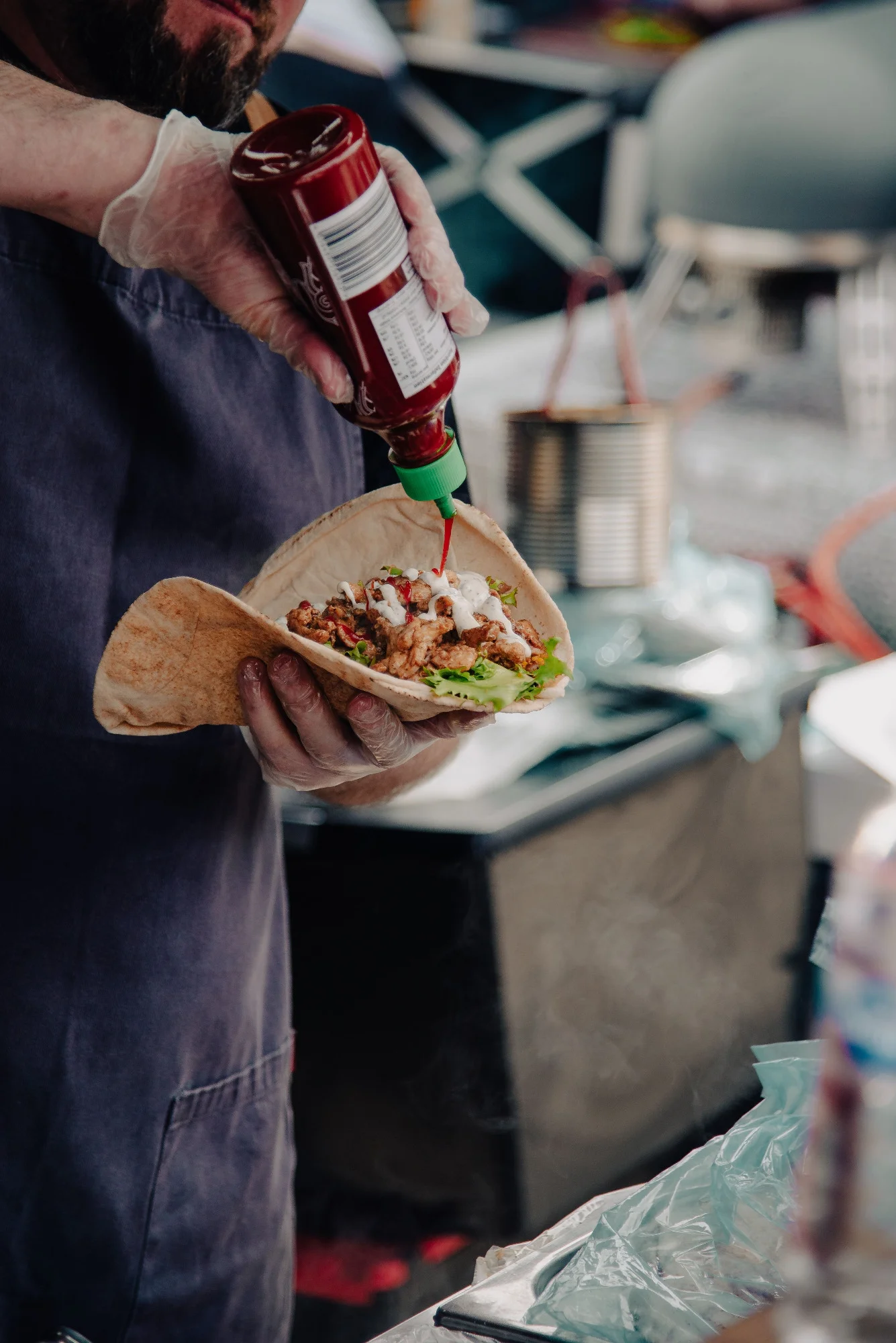 A chef in a food truck adding sauce to a freshly made taco, capturing the bustling atmosphere of street food preparation.