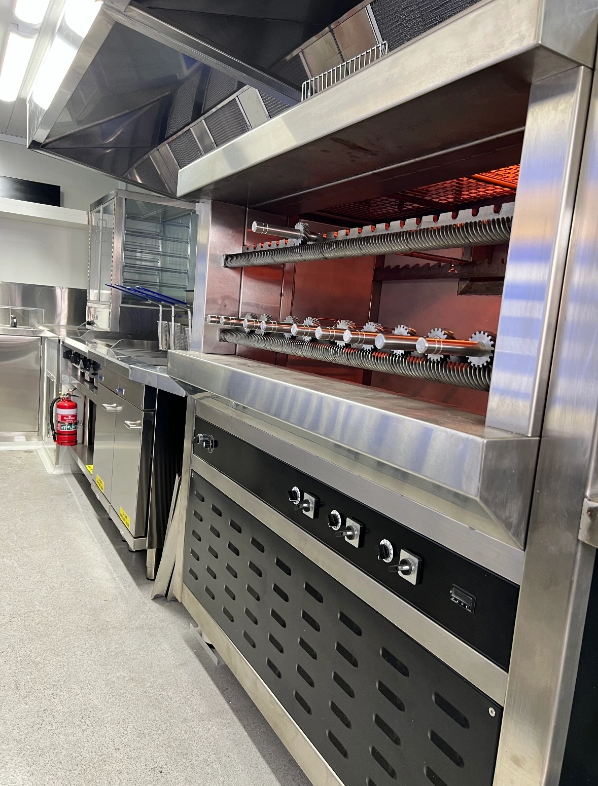 Close-up of a grill station inside a Greek food truck, featuring rotisserie skewers and a ventilation hood.