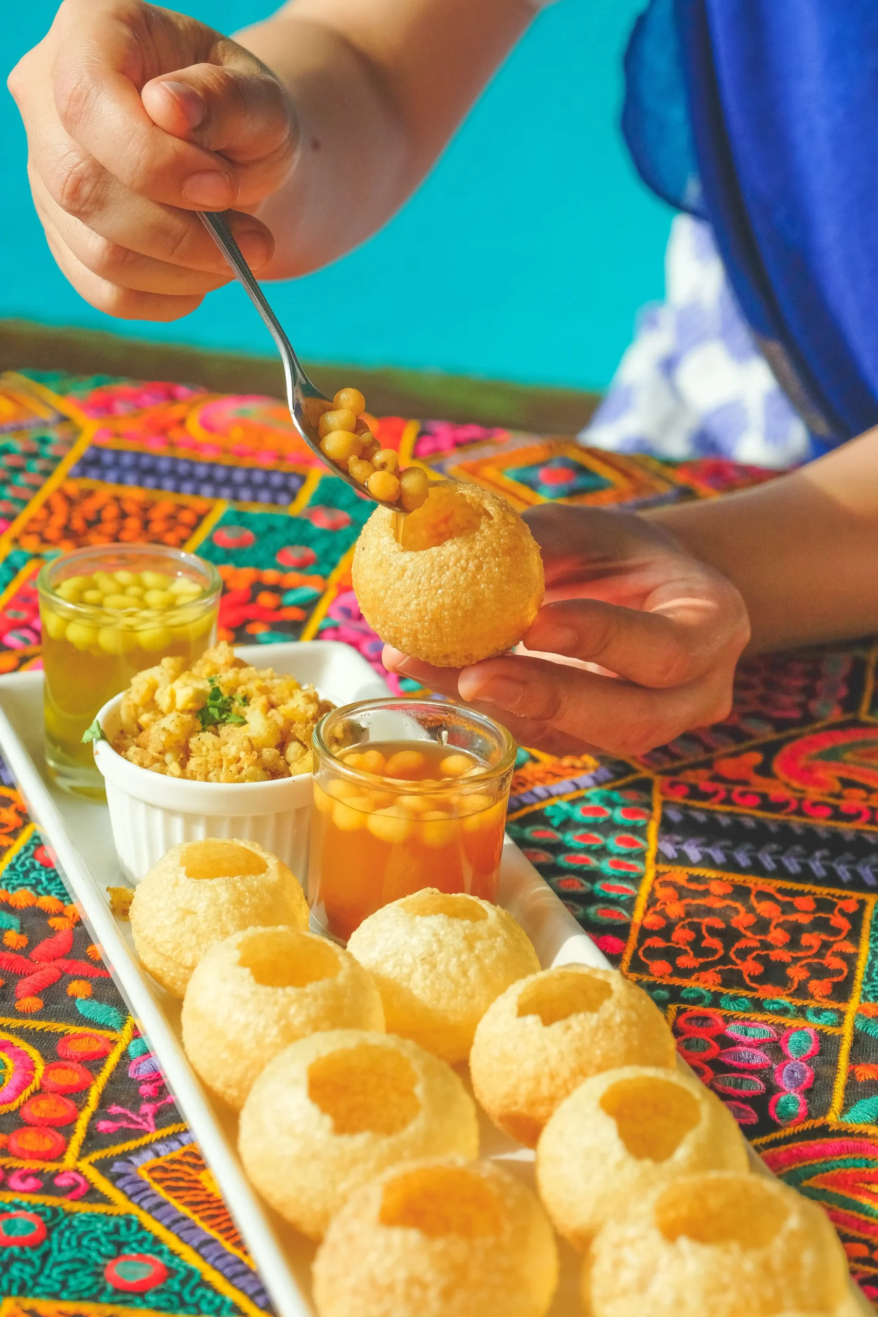 Traditional Indian street food Pani Puri, served with tamarind water, chickpea masala, and spicy green chutney, on a colorful embroidered tablecloth from indian food truck.